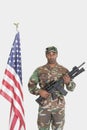 Portrait of US Marine Corps soldier with M4 assault rifle standing by American flag over gray background Royalty Free Stock Photo