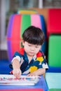 Portrait vertical image of baby boy picking up chalk colors for crafting on the table. Son doing art on white paper. Happy child