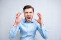 Portrait of very angry, annoyed, wild man shouting, yelling, holding hands near face, standing over grey background Royalty Free Stock Photo