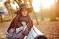 Portrait of a very beautiful young brunette woman with shiny straight hair in a gray coat and black hat, sitting on a bench on th Royalty Free Stock Photo