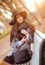 Portrait of a very beautiful young brunette woman with shiny straight hair in a gray coat and black hat, sitting on a bench on th Royalty Free Stock Photo