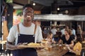 Portrait Of Waiter Serving Food To Customers In Busy Bar Restaurant