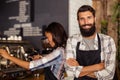 Portrait of waiter standing with arms crossed while waitress working in background Royalty Free Stock Photo