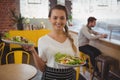 Portrait of waitress holding plates with salad while businessman using laptop