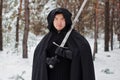 Portrait of a warrior in black quilted clothes, leather gloves, a cloak with a hood and a sword in his hands