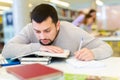 Portrait of upset adult man with stack of books on table in room of public library