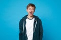 Portrait of weird young man in casual clothes keeping eyes closed screaming isolated on blue wall background in studio Royalty Free Stock Photo