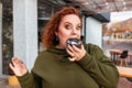 Portrait of a well-fed surprised woman eating a shocking chocolate donut. The concept of diet and obesity