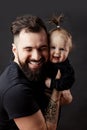 Handsome tattooed young man holding cute little baby on black background