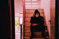 Portrait of white mask and hoodie sitting on old stairs. Selective focus on hands. Sadness, despair, dark, concept