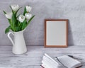 Portrait white picture frame mockup on table with tulips jug vase and open busines diary book concrete wall background. Royalty Free Stock Photo