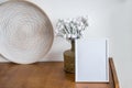 Portrait white picture frame mockup on wooden table. Modern ceramic vase with withe frowers