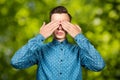 Portrait White young man dressed in blue shirt, closes eyes his hands. Man on green bokeh background Royalty Free Stock Photo