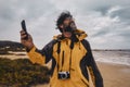 Portrait of wild photographer enjoying bad weather at the beach. Happy tourist with photo camera and mobile phone. Beach and ocean Royalty Free Stock Photo