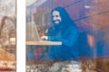 Portrait through the window of handsome young adult man freelancer in casual style sitting in cafe, chating with his friend in Royalty Free Stock Photo