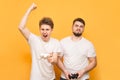 The portrait of the winner and losers are with joysticks in their hands on a yellow background. Two emotional men play video games