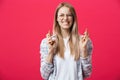 Portrait of wishful young woman in casual clothes with blonde dyed hair, crossing her fingers, biting her lower lip