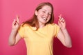 Portrait of wishful young woman in casual yellow t sirt, with brown hair, crossing her fingers, hopes before important event, Royalty Free Stock Photo