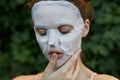 Portrait of a woman anti-aging mask holds a finger near the lips and closed eyes bare shoulders leaves in the background Royalty Free Stock Photo