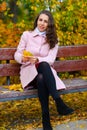 Portrait of a woman in an autumn park. She is sitting on a bench with yellow maple leaves Royalty Free Stock Photo