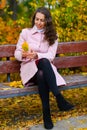 Portrait of a woman in an autumn park. She is sitting on a bench with yellow maple leaves Royalty Free Stock Photo