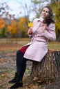 Portrait of a woman in an autumn park. She is sitting on a stump. Beautiful trees with yellow leaves