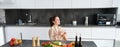 Portrait of woman in bathrobe sitting in kitchen with smartphone, cooking dinner, watching recipe on social media, video