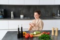 Portrait of woman in bathrobe sitting in kitchen with smartphone, cooking dinner, watching recipe on social media, video