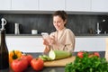 Portrait of woman in bathrobe sitting in kitchen with smartphone, cooking dinner, watching recipe on social media, video