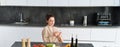 Portrait of woman in bathrobe sitting in kitchen with smartphone, cooking dinner, watching recipe on social media, video