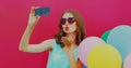 Portrait of woman blowing her red lips sending sweet air kiss taking selfie picture by smartphone with colorful balloons on pink Royalty Free Stock Photo