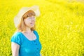 Portrait woman in blue dress and straw hat walk in yellow colza field