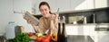 Portrait of woman checking recipe notes in notebook, standing in kitchen with vegetables, cooking food, preparing Royalty Free Stock Photo