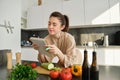 Portrait of woman checking recipe notes in notebook, standing in kitchen with vegetables, cooking food, preparing Royalty Free Stock Photo