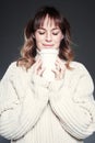 Portrait of woman with closed eyes wearing sweater holds a paper disposable coffee cup. Drinking coffee, look straight to camera