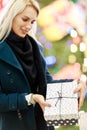 Portrait of woman in coat with gift box on background of Christmas tree in store Royalty Free Stock Photo