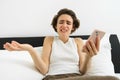 Portrait of woman with confused face, laying in bed with smartphone, chatting on mobile phone app, video call, shrugging
