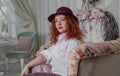 Portrait A woman in a burgundy hat in a beautiful interior sits on beautiful sofas and looks at the camera. Delicate Home Decor