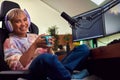 Portrait Of Woman Gaming At Home Drinking Coffee Sitting At Desk With Monitors