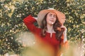 Portrait of a woman in the garden. A young and beautiful woman in a red dress holds a straw hat with her hand Royalty Free Stock Photo