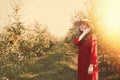 Portrait of a woman in the garden. Young and beautiful woman in a red dress and a straw hat, straightens her hair. Hot weather. Royalty Free Stock Photo