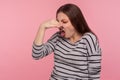 Portrait of woman grimacing with disgust, holding breath, pinching nose with fingers to avoid bad smell