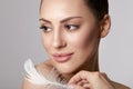 Portrait of woman with large white feather near beauty face and perfect skin on gray background. Skin care.