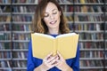 Portrait of woman in a library with opened book hold in hands, long hair. Young college student girl in co-working