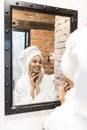 Portrait of beautiful woman looking into mirror in bathroom applying cream on face, healthy grooming skin care cosmetics