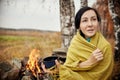 Portrait of a woman with a mug of hot tea in his hands autumn in a forest campfire. A picnic in the autumn forest. Girl wrapped Royalty Free Stock Photo