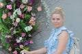 Portrait of a woman near the flowers on the facade of the building. A woman leans on the steering wheel of a bicycle. Looking away