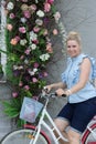 Portrait of a woman near the flowers on the facade of the building. A woman leans on the steering wheel of a bicycle. Looking away
