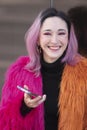 Portrait of a woman with pink hair wearing a fluffy colorful jacket ad using her phone outdoors Royalty Free Stock Photo