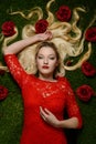 Portrait of woman in red dress laying in grass with roses Royalty Free Stock Photo